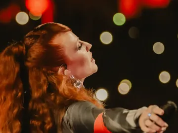 Jess Glynne in front of sparkly light with a mic in her hand