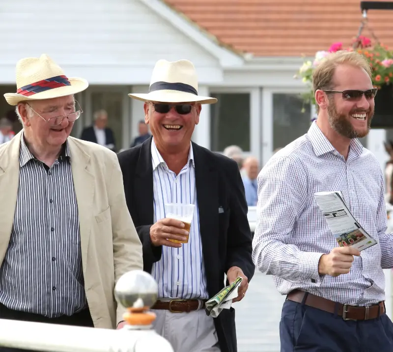 Three men smiling at the racecourse.