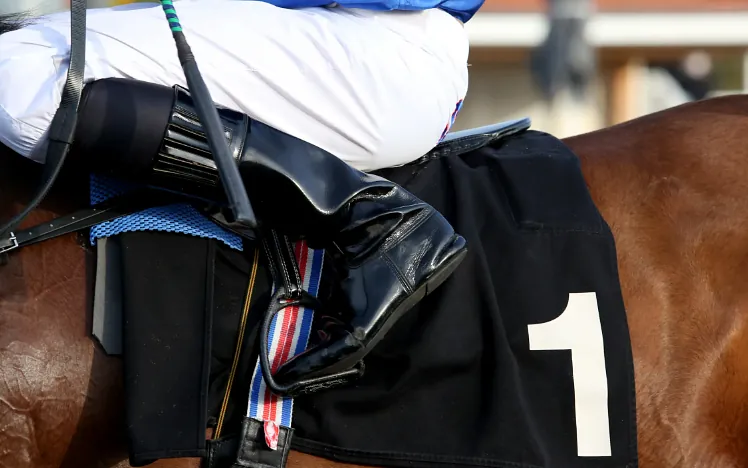 A close up of a horse's saddle and jockeys boot.