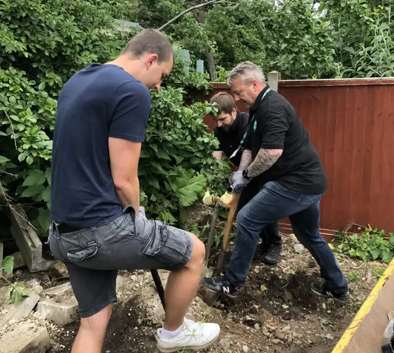 Three men digging into garden ground.